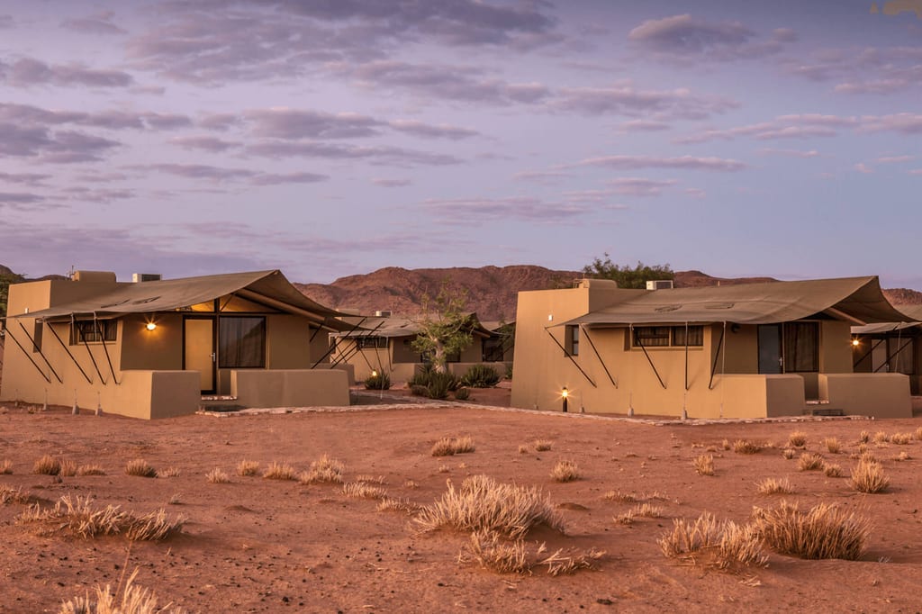 Zwei sandfarbene Lodges in trockener Wüstenlandschaft bei Abenddämmerung
