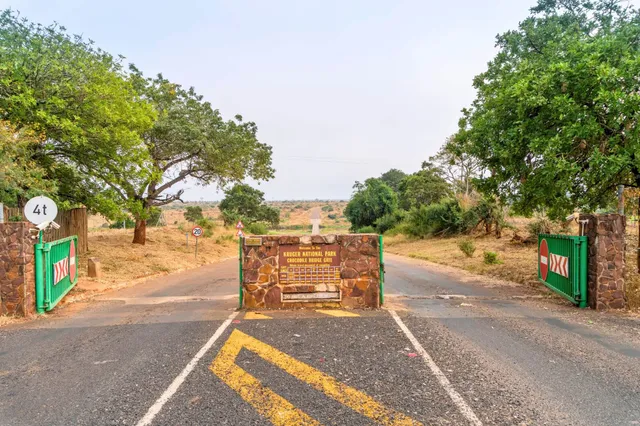 Frontansicht eines Parkeingangs mit Steinbarriere und grünen Toren vor trockener Savannenlandschaft