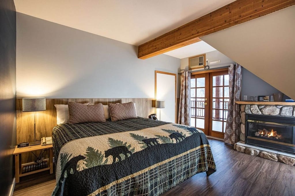 Gemütliches Hotelzimmer mit großem Bett, Kamin, Holzbalken und warmer Beleuchtung.
