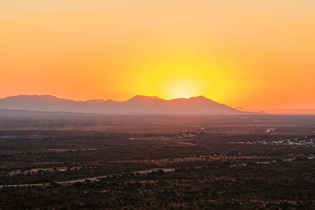 Weite Savanne bei Otjiwarongo, Namibia, mit Sonnenaufgang über Bergen und warmem Orangeton.