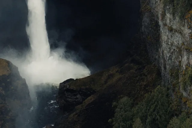 Wasserfall stürzt in enge Schlucht, Gischt steigt vor steilen Felswänden und bewaldeten Hängen auf.