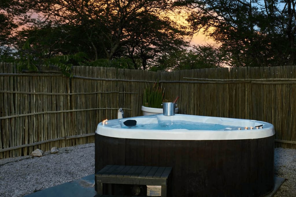 Outdoor-Whirlpool mit Kerzen und Sektkühler bei Sonnenuntergang hinter Staketenzaun