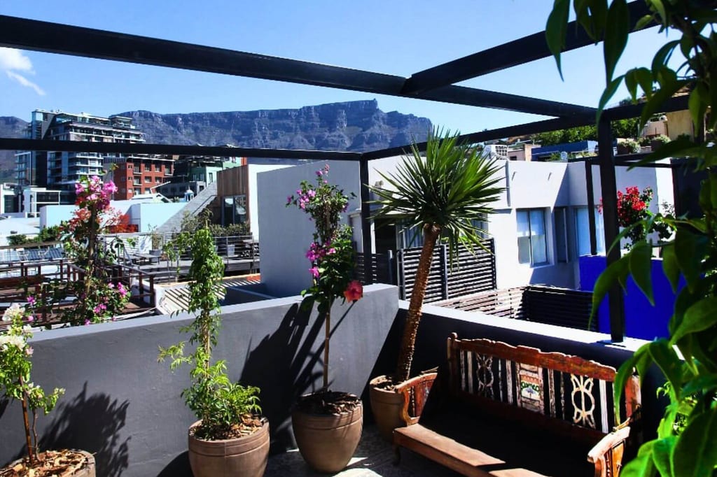 Sonnige Dachterrasse mit Topfpflanzen, Holzbank und Bergmassiv im Hintergrund