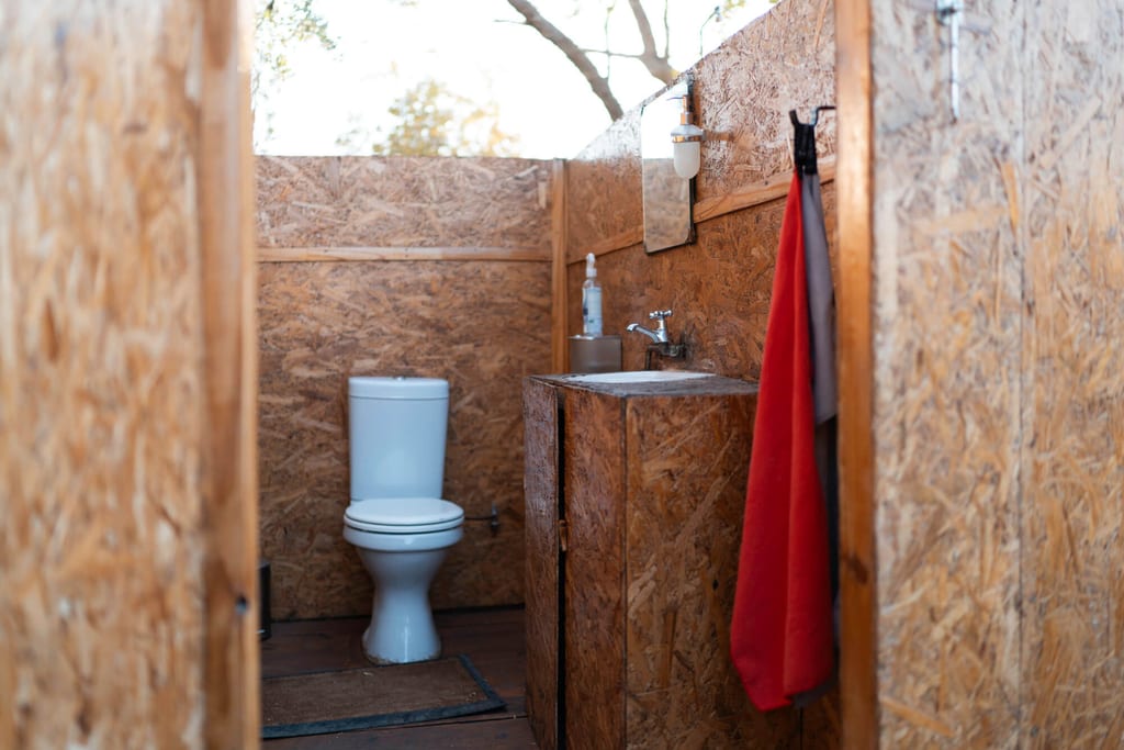 Offene rustikale Toilettenanlage mit WC, Waschbecken und rotem Handtuch in OSB-Holzwänden
