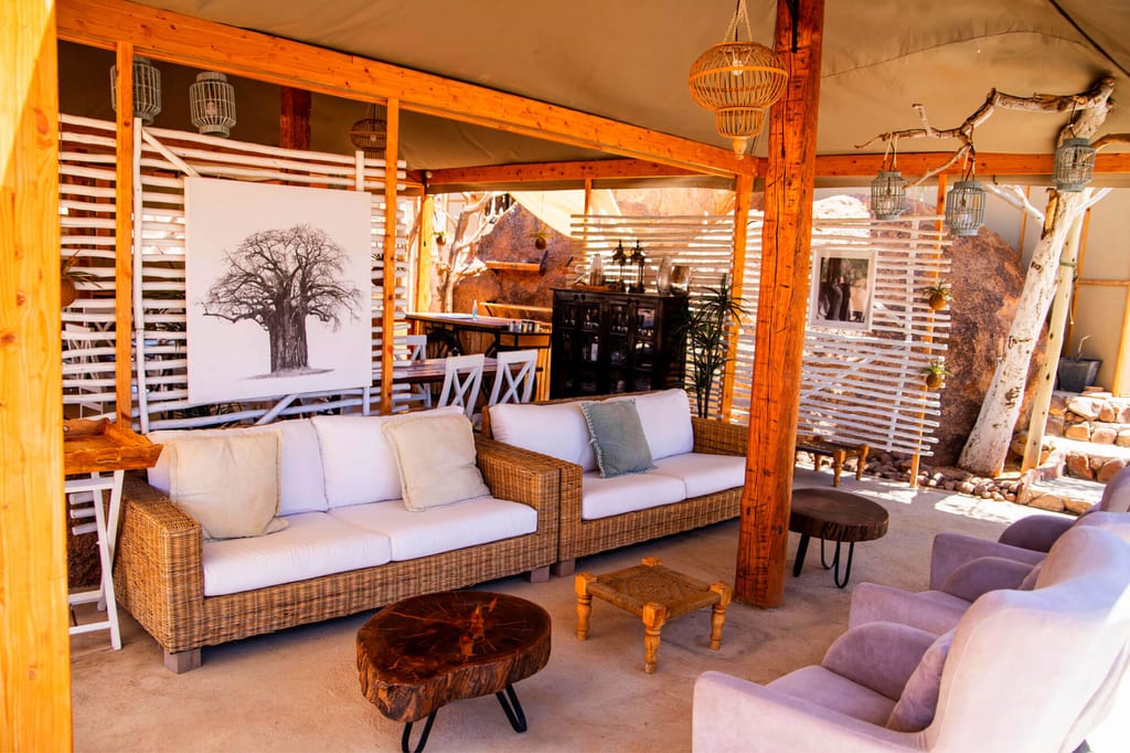 Gemütliche Freiluft-Lounge mit Rattansofas, Polstersesseln und Holzelementen in warmem Tageslicht.