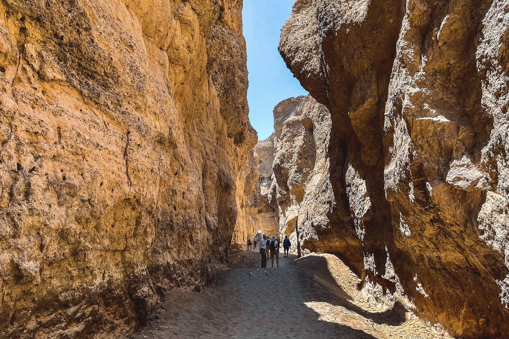 Enge Sandsteinschlucht mit Wanderern, sonnige Felswände und tiefe Schatten.