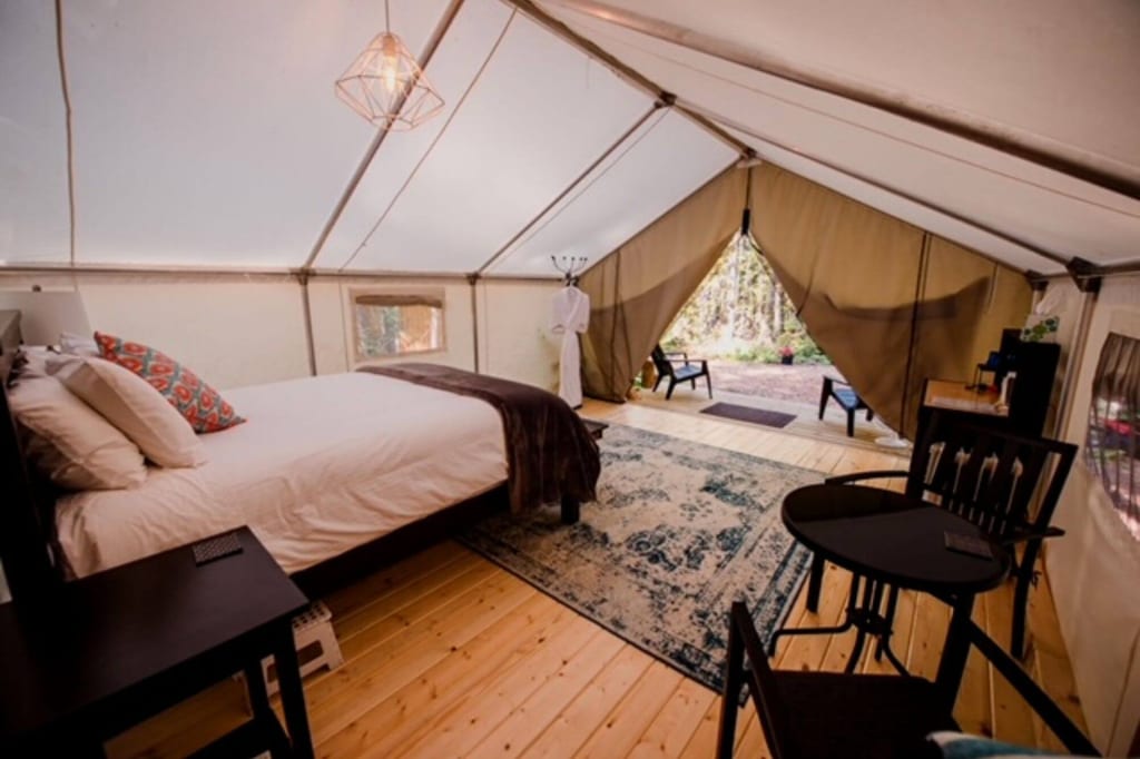 Gemütliches Glamping-Zelt mit Bett, Teppich und offener Veranda im Tageslicht