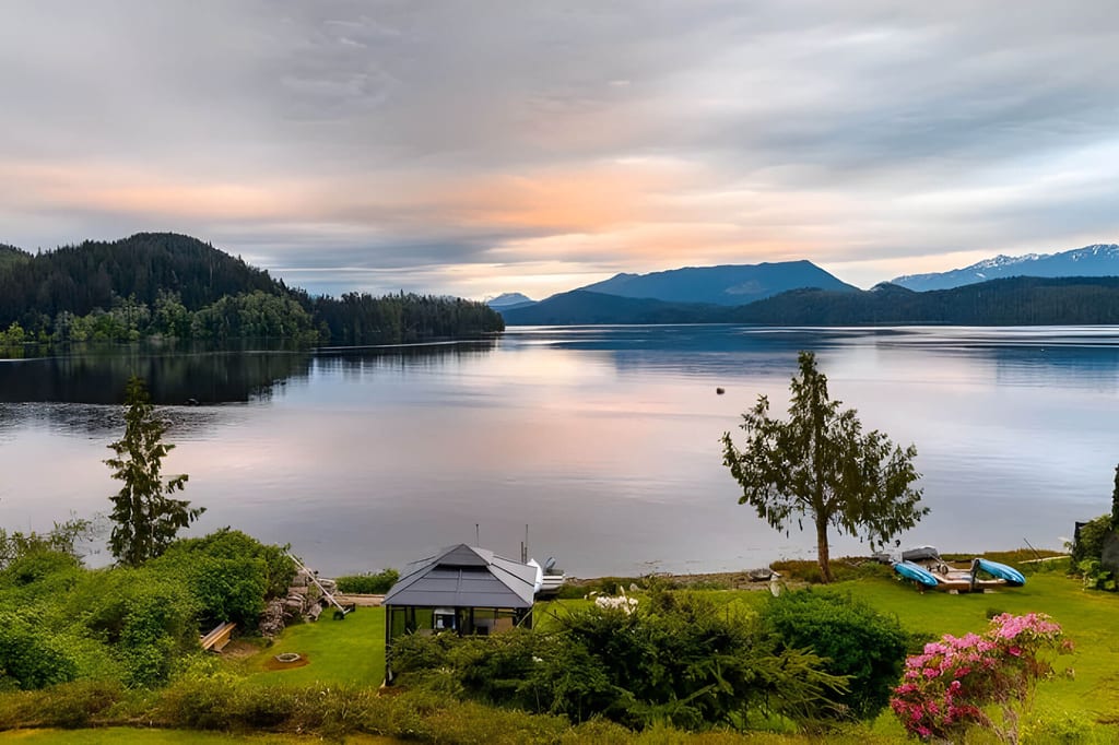 Dämmerungsblick über ruhigen See mit Pavillon, Booten und Bergen im Hintergrund, pastellfarbener Himmel