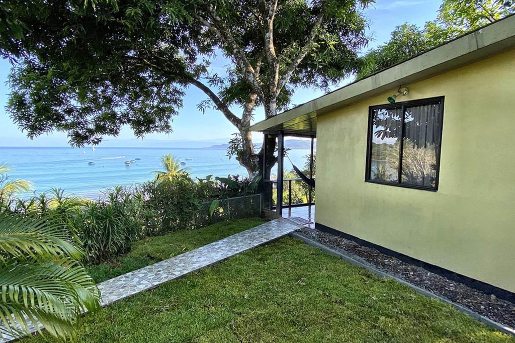 Gelbes Haus mit Hängematte im Garten und Blick auf ruhige See mit Booten