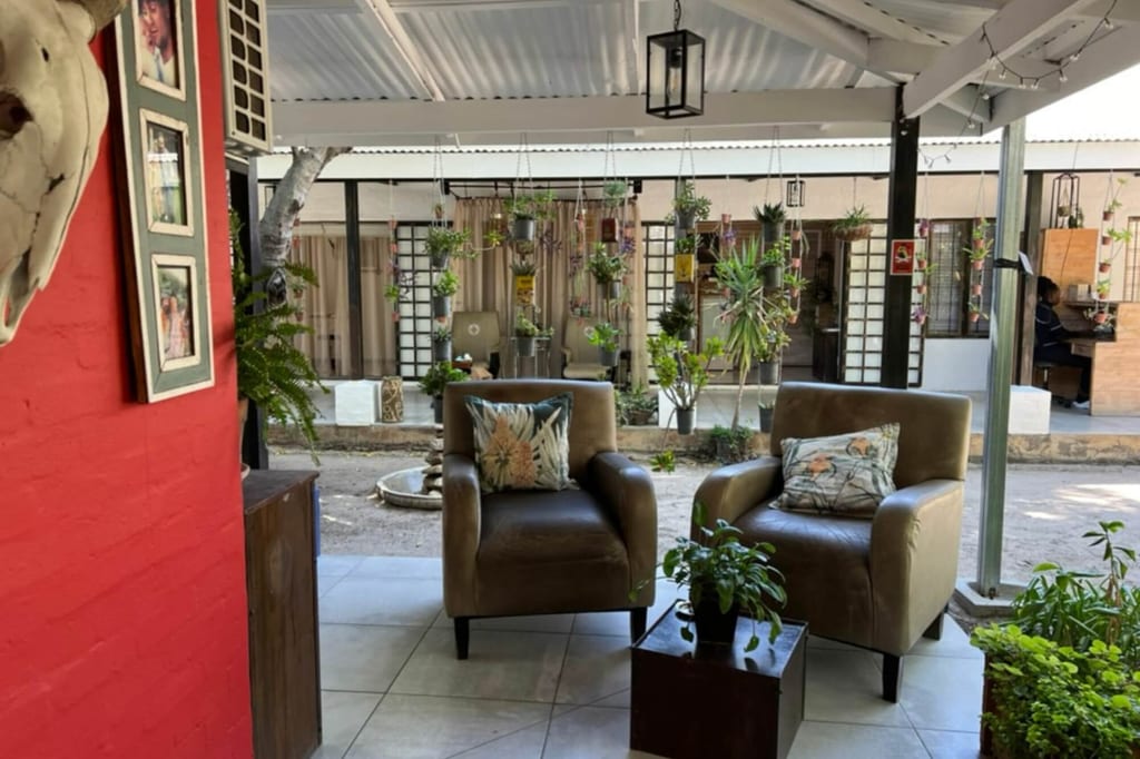 Überdachte Terrasse mit zwei Sesseln, vielen hängenden Topfpflanzen und ruhiger Tageslichtstimmung
