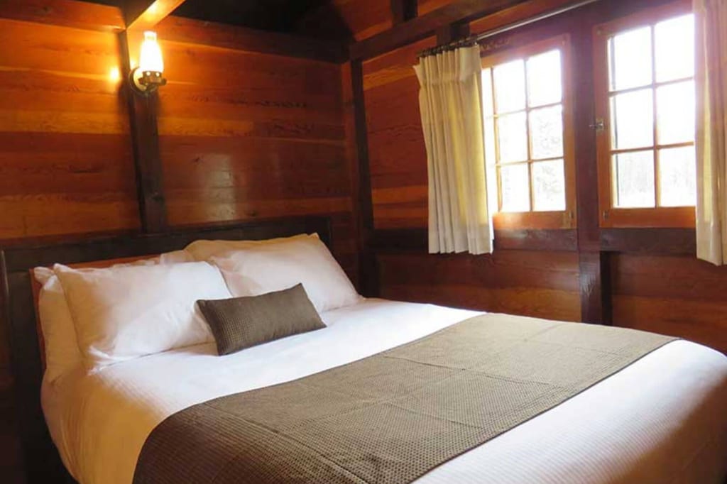 Gemütliches Schlafzimmer in Holzhütte mit weiß bezogenem Doppelbett und warmem Licht.