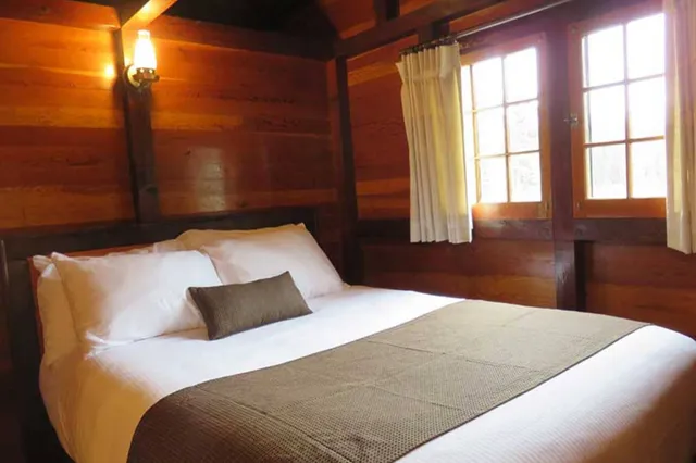 Gemütliches Schlafzimmer in Holzhütte mit weiß bezogenem Doppelbett und warmem Licht.