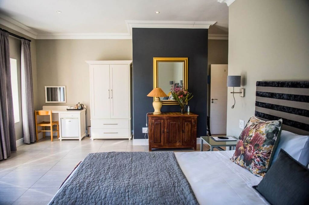 Helles, aufgeräumtes Hotelzimmer mit Doppelbett, Garderobe und Holzdresser unter Tageslicht.