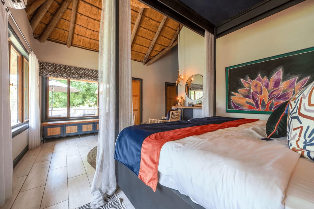Helles Schlafzimmer mit Himmelbett, Reetdach und großen Fenstern mit Blick ins Grüne.