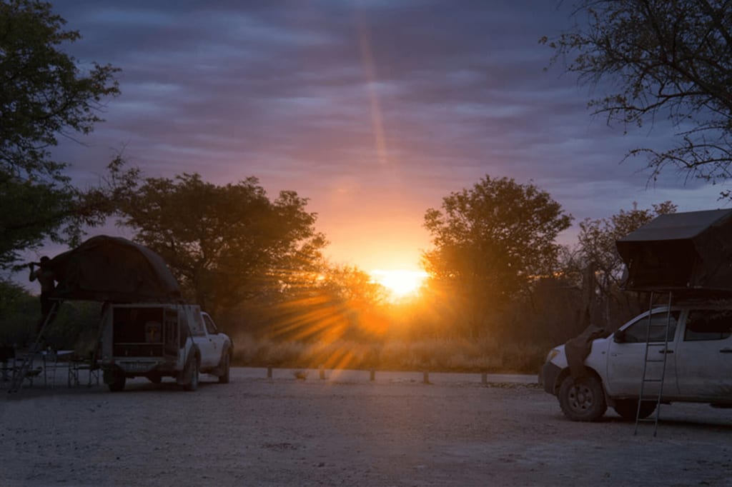 Zwei Geländewagen mit Dachzelten bei Sonnenuntergang auf staubigem Campingplatz