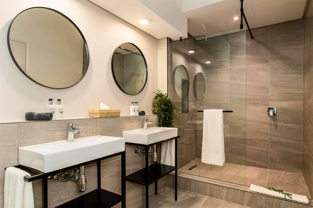 Modernes Badezimmer mit zwei Waschbecken, runden Spiegeln und einer großen Glasdusche