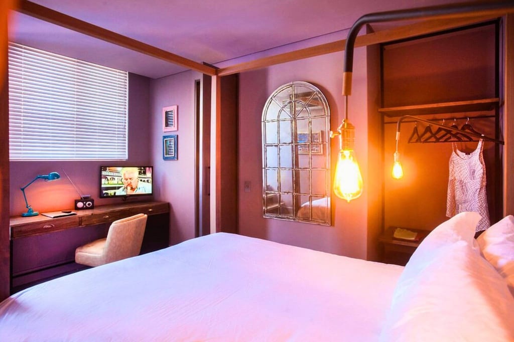 Gemütliches Hotelzimmer mit großem Bett, Schreibtisch, offenem Kleiderschrank und warmen Hängelampen.